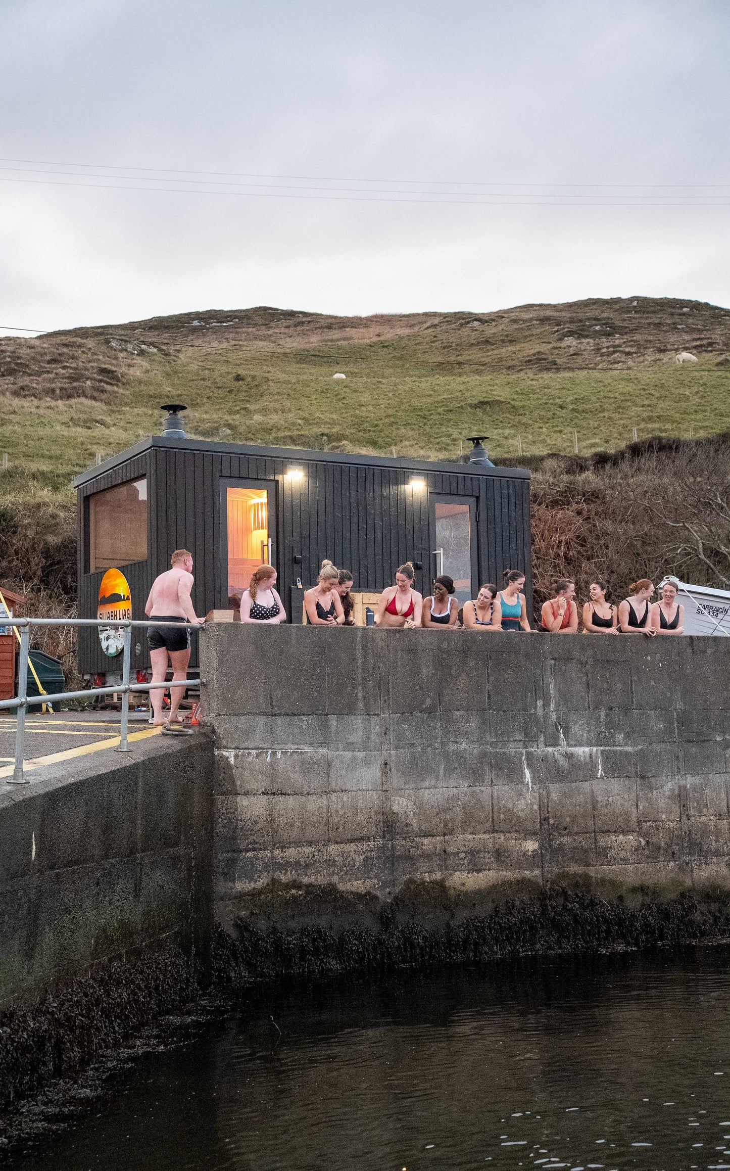 Group of guests outside the bespoke double wood-fired Sliabh Liag Sauna at Teelin Pier, preparing for a sea plunge.