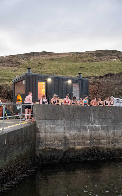 Group of guests outside the bespoke double wood-fired Sliabh Liag Sauna at Teelin Pier, preparing for a sea plunge.