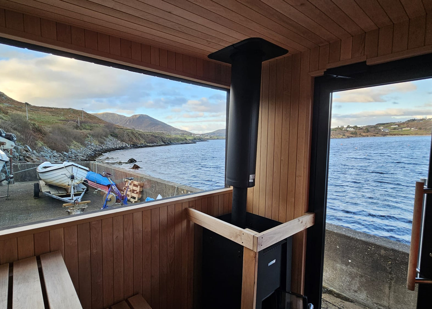 Interior of the bespoke double wood-fired Sliabh Liag Sauna showing panoramic coastal views of Teelin Bay and the surrounding hills.