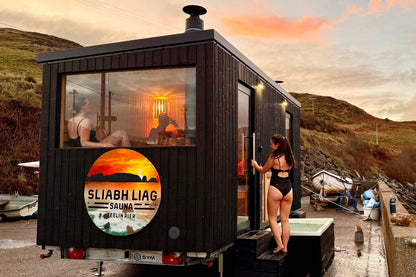 Guests enjoying the bespoke double wood-fired Sliabh Liag Sauna and cold plunge at Teelin Pier during a colourful sunset.